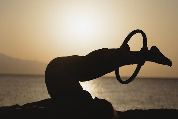 Person doing sun salutation yoga sequence outdoors at sunrise.